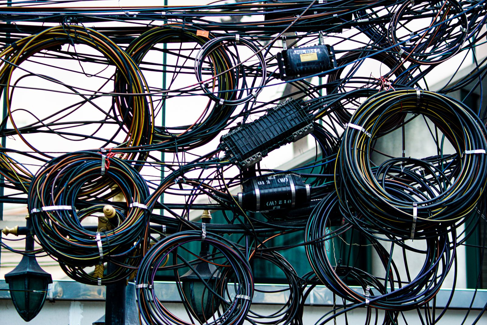 Tangled overhead wires and large coils of cable outside a building.