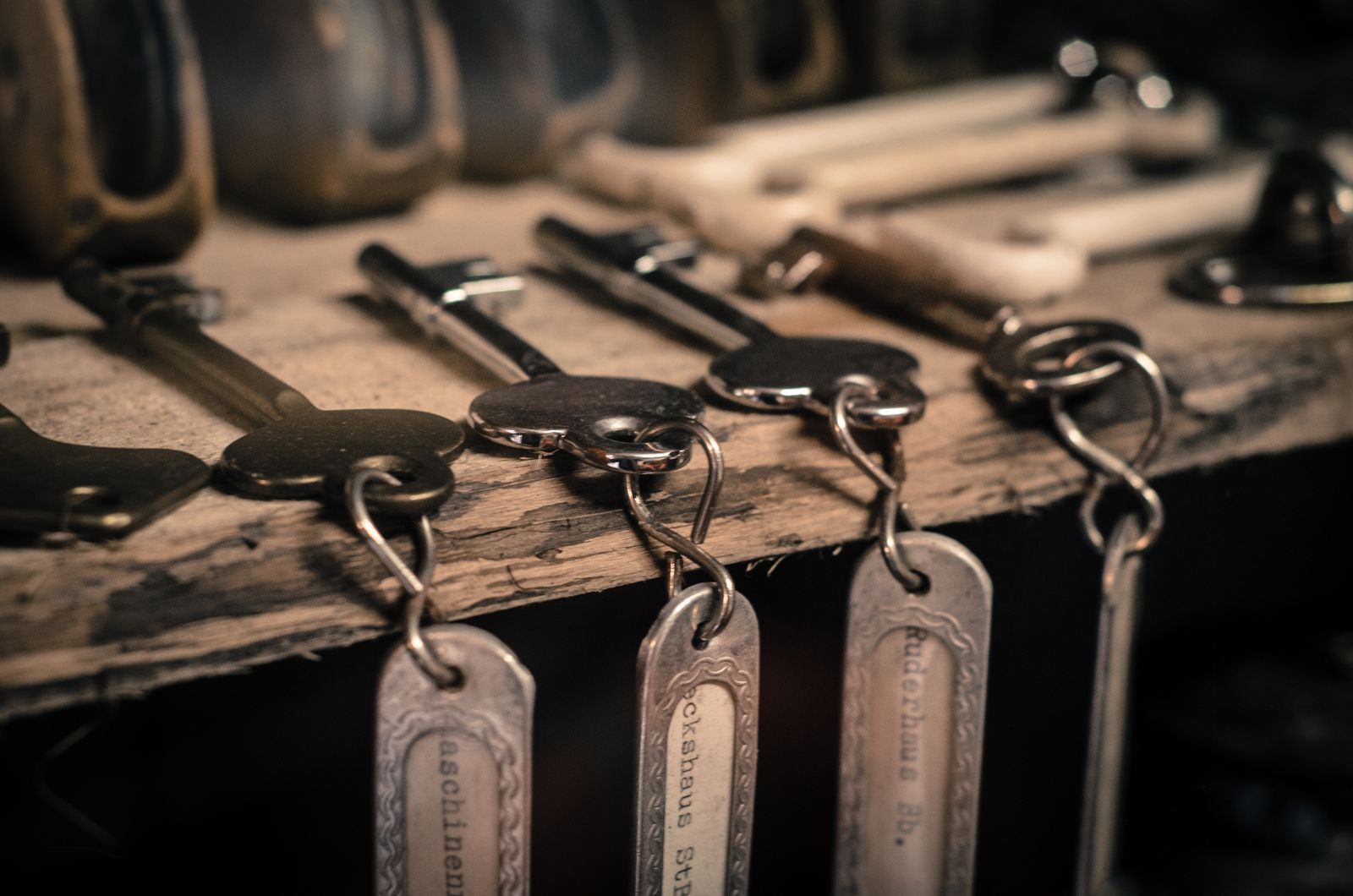 Antique keys with labeled metal tags hanging from the edge of a rustic wooden shelf.