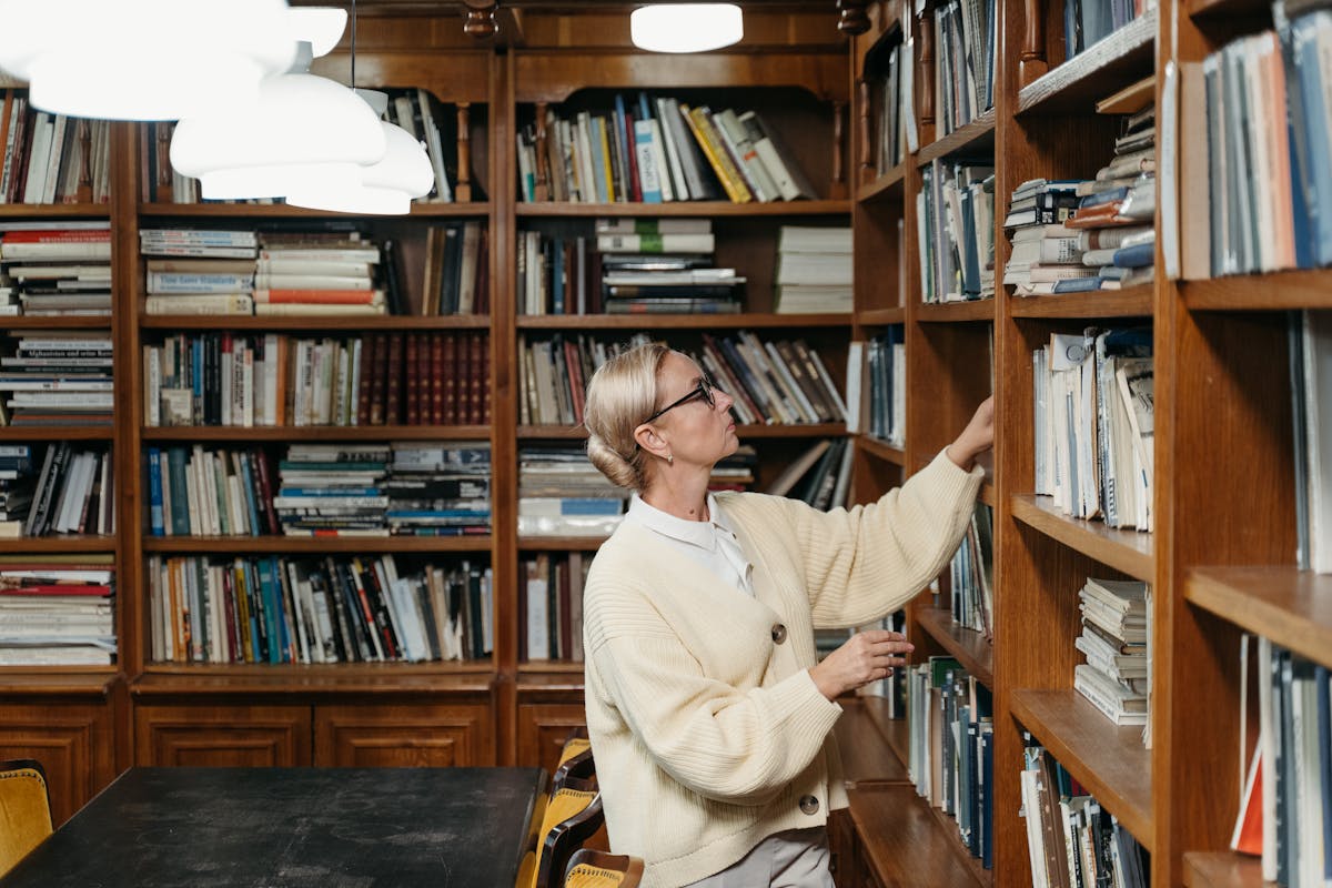 A woman choosing a book in a library aisle.
