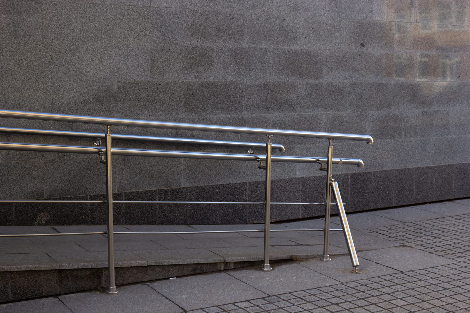 A metal handrail beside an accessibility ramp on a city sidewalk.